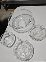 Four vintage glass pieces on white surface showing beaded edges and hobnail pattern, including a large bowl and smaller dishes with handles.