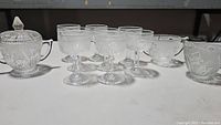 Full set showing covered sugar bowl with lid and handles along with eight stemmed glasses, all clear glass with Iris pattern.