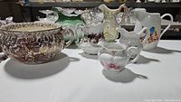 Overview of all 8 vintage porcelain pitchers with varied designs and minor chipping.