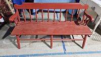 Full view of the vintage red wooden bench showing the seat, backrest with vertical spindles, and armrests.