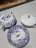 Three vintage porcelain serving bowls with lids, showing blue and white floral pattern on one and pastel leaf motif with gold knob on another.