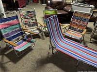 Five aluminum frame folding beach chairs arranged in a garage-like setting showing different colorful fabric patterns and wooden armrests.