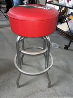 Side view of red vinyl padded barstool seat with chrome metal legs and footrest, showing condition and structure