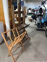 Photo showing both the World Market dual easel and Utrecht canvas storage rack placed on the floor in a basement-like setting with other furniture and equipment in background.