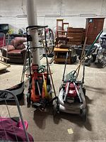 Photo showing Honda gas lawnmower, Black & Decker electric mower, and weedwacker resting on a concrete floor with other garden tools partially visible