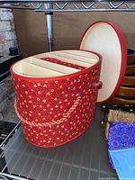 Oval red fabric jewelry case with lid off showing interior compartments and braided exterior handle