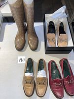 Top-down photo showing all four shoes: three pairs of loafers (tan and red leather, silver horsebit detail) and a pair of knee-high beige rain boots with brown logo pattern.
