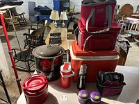 Full view of the lot showing various coolers, a lobster-themed black speckled enamelware stock pot with lid, and multiple insulated thermoses and containers on tables.