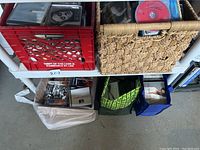 Wide view of various containers holding many CDs including a red plastic crate and woven basket under a metal shelf.