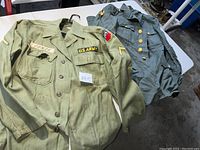 U.S. Army jacket olive green color with patches and creased fabric, displayed on a table with other clothing
