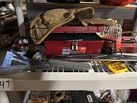 Overall lot displayed on a shelf showing a tool belt, red Stack-On toolbox, various hand tools including pry bar, scraper, file, screwdriver, sharpening stone, soldering iron.