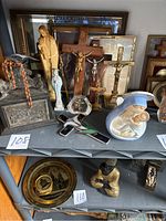 Photo of various crucifixes, statues, rosary beads, and religious box placed on shelf showing arrangement and condition