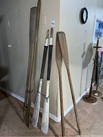 Full view showing all three sets of wooden oars leaning against a wall, highlighting lengths and general worn conditions