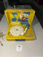 Photo showing the open phonograph with yellow casing and graphic of Donald Duck inside the lid. Donald's arm rests on the turntable platter as the needle.