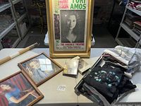 Top-down view of all lot items on table: framed prints, framed poster, video media and folded t-shirts