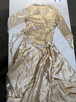 Full view of vintage ivory silk or satin 1920s wedding dress laid flat showing long sleeves, fitted waist, and flowing skirt.