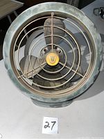 Front view of green vintage Vornado fan showing metal protective grille and blades with dust and rust.