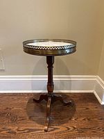 Full front view of round marble top table with brass gallery and wood pedestal base