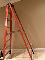 Side angle photo showing the full 8-foot height of the orange fiberglass ladder with metal rungs and black rubber feet on the floor.