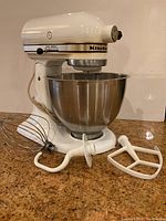 Front view of white KitchenAid stand mixer with bowl and three attachments arranged in front