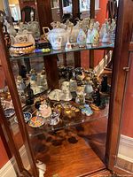Full view of two upper shelves showing porcelain pitchers, creamers, small figurines and decorative bowls