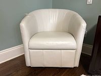 Front view of white leather swivel armchair on wood floor, showing seat cushion and channel-stitched back