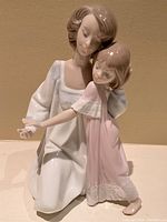 Front and angled view of the Lladro porcelain figurine showing mother in white gown kneeling and embracing daughter in pink nightgown.