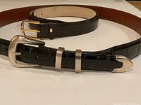 Black and brown alligator leather belts coiled side by side, buckles visible