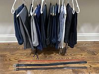 Full view of 14 pairs of pants hanging and 3 belts laid flat