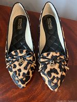 Top down view of pair of leopard print Michael Kors slip-on flats showing the black quilted interior and front bow with MK charm.