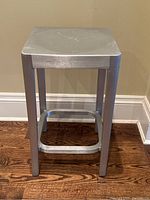 Front view of stool showing square seat, legs, and footrest