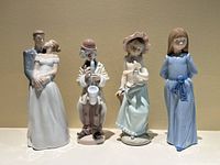 Front view of four porcelain figurines: Lladro couple and three Nao figurines including a clown, a girl in hat, and a girl in blue dress