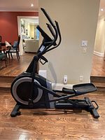 Side profile view of the elliptical showing full frame and flywheel housing on hardwood floor.