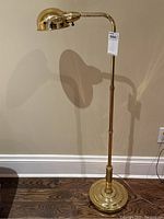 Full view of the brass Mid-Century Modern style floor lamp standing on wood floor against wall, showing height and base details.
