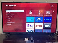 Front view of 40-inch TCL Roku TV powered on displaying Roku home interface with remote placed in front on table.