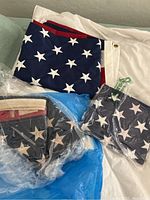 Four American flags folded, some wrapped in plastic, showing blue field with white stars and red and white stripes.