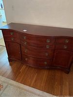 Front view of the antique mahogany buffet showing its curved design, eight drawers, and two cabinet doors with metal Hepplewhite style knobs.