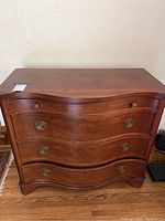 Front view of small antique mahogany dresser with curved fronts and brass Hepplewhite pulls.