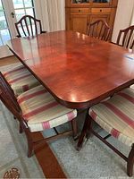 Photo showing full view of antique mahogany dining table with five wooden dining chairs with striped cushioned seats and one captain chair with armrests.
