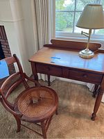 Desk, cane chair, and lamp in a room near window, showing overall condition and placement.