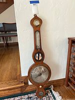 Full view of the antique wooden barometer showing its elongated shape with barometer, thermometer and hygrometer sections.