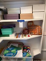 Shelf containing multiple gift boxes in neutral and pastel colors, orange holiday decoration, holiday stickers, and various spools of yarn and ribbon.