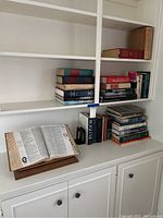 Bookshelves featuring an open book on wooden adjustable book stand, stacks of coffee table books, and two black metal book ends holding upright books.