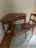 Full view of the wooden corner desk with drawer and the wooden chair with cane seat next to it showing the overall condition and style.