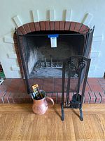 Black metal mesh fireplace screen in front of brick fireplace with black metal fireplace tool stand and copper pitcher on floor