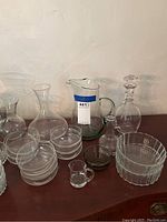 Overview of assorted clear glassware including decanter, pitchers, bowls, and vases on a wooden surface