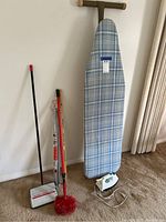 Photo showing full lot leaning against wall including ironing board with iron, carpet sweeper, red duster, two clothes rods, and yardstick