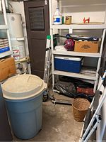 Full view of storage room showing shelves, blue trashcan, ladder, scooter, and wastebasket.