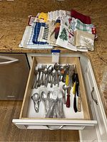 Kitchen towels folded on countertop and drawer open showing various silverware and utensils inside.