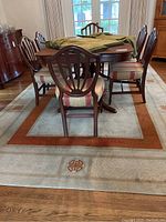 Dining table with chairs placed on top of the large Asian influenced rug showing its size and colors rust and tan.